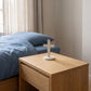 Petite croix de 13 cm sur une table de chevet en chêne, chambre aux draps bleus