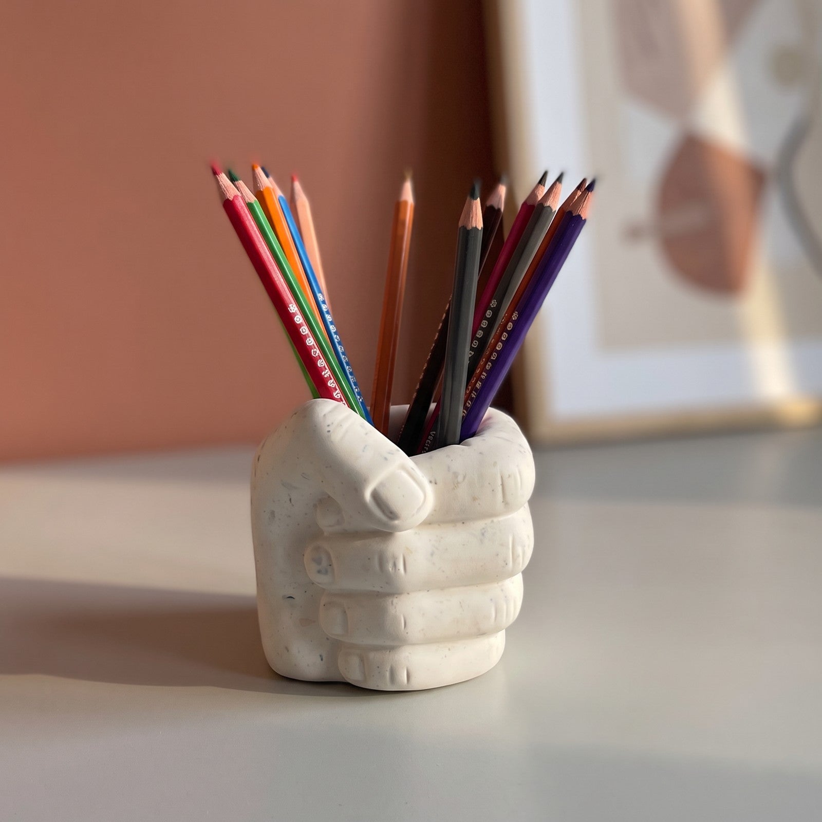 Pot à crayons Main avec crayons de couleur dans un espace dessin, sur un bureau gris devant un mur terracotta